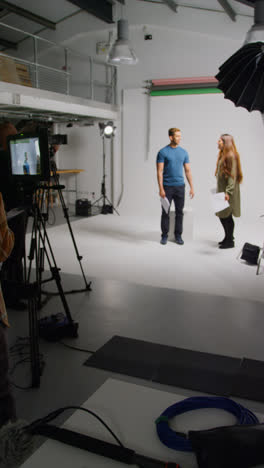 Vertical-Video-Of-Actors-With-Scripts-In-Rehearsal-Shooting-Movie-Or-Video-In-Studio-With-Female-Director-And-Film-Crew-And-Watching-On-Monitor